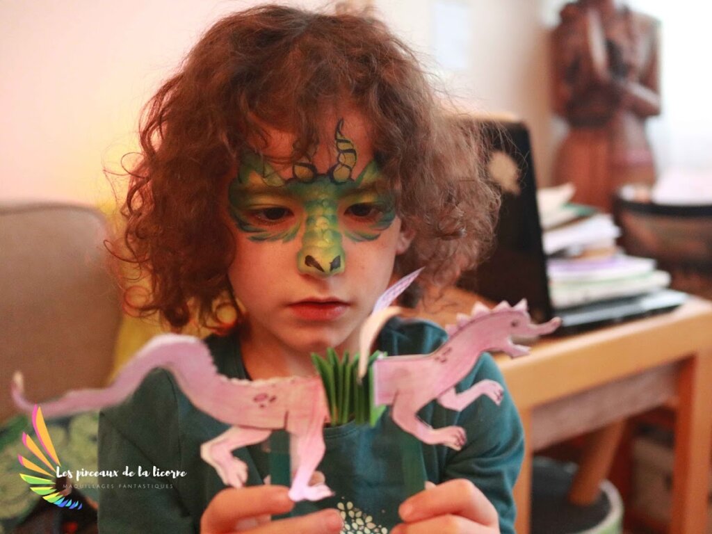 Une petite fille maquillée joue avec un bricolage de dragon lors d'un anniversaire enfant créatif à Lorient